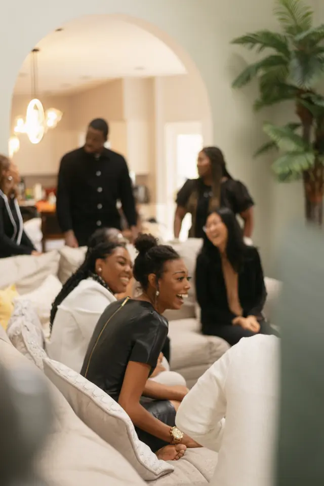 Seen through an arched doorway, Black women laugh together on a sofa.