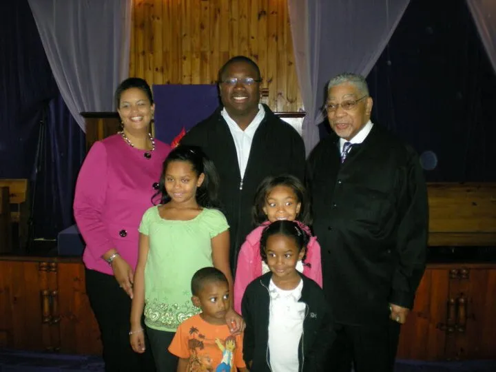 Young Nicole with her family, standing beside an AME bishop in his robe at the front of a church.