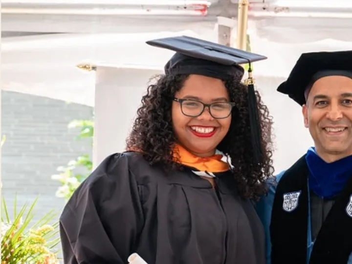 Nicole in cap and gown, smiling with her diploma beside a professor in academic robes.