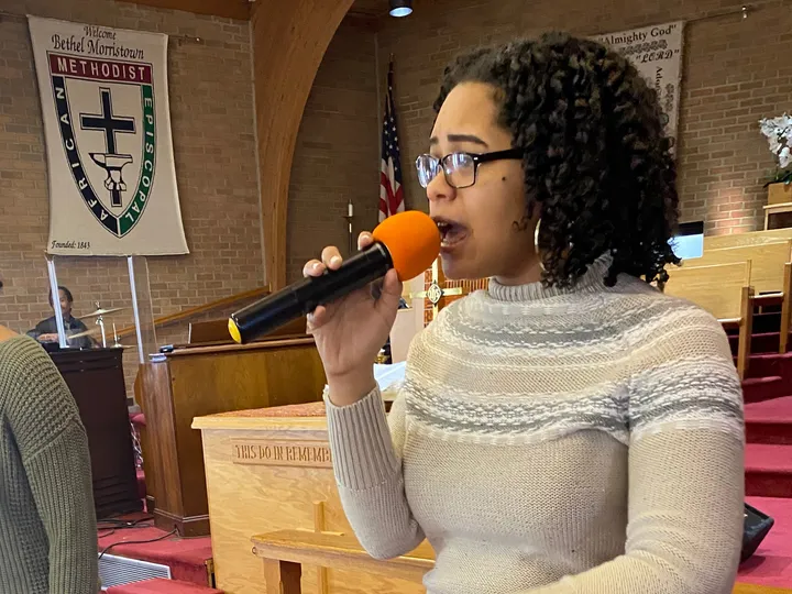 Nicole sings into a microphone at the front of a church, leading worship.