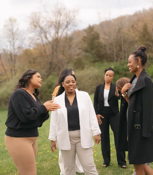 Black women stand close together on a lawn, one with her hand on a sister's shoulder, smiling.